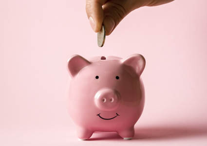 Hand dropping coin into pink piggy bank